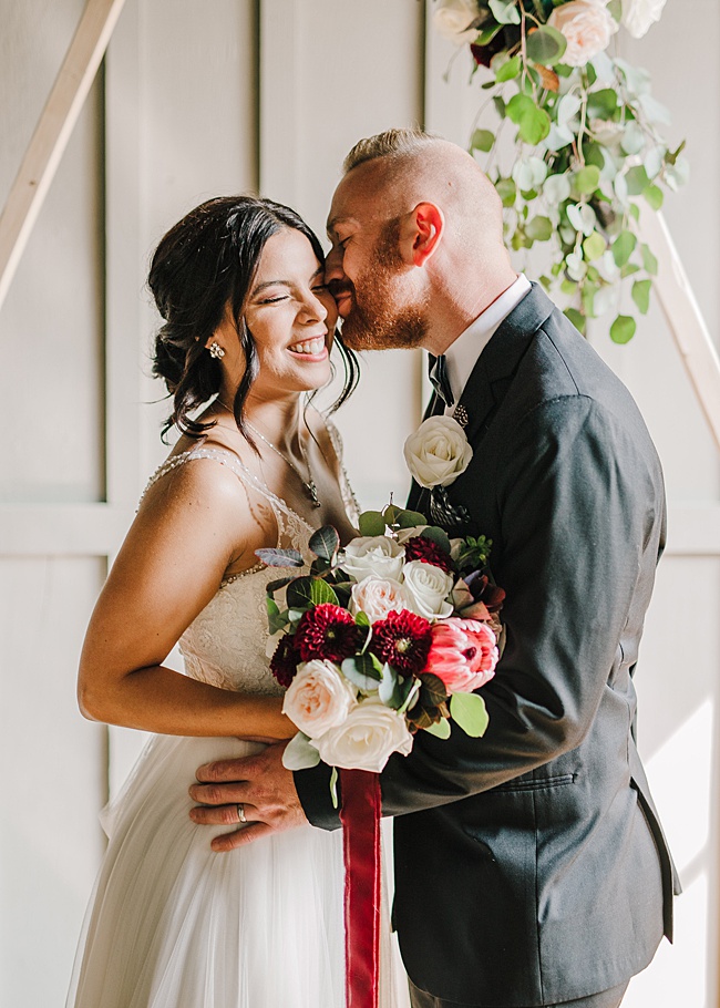 bride and groom kiss with peek at custom jadorn designs botanical earrings and necklace