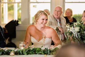 Bride seated at her wedding reception, bride wears sparkly gold bridal teardrop earrings by J'Adorn Designs bridal jeweler for a classic Annapolis wedding at Chesapeake Bay Beach Club
